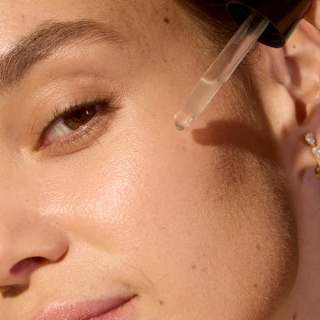 Close-up of a person applying a skincare dropper to their face.